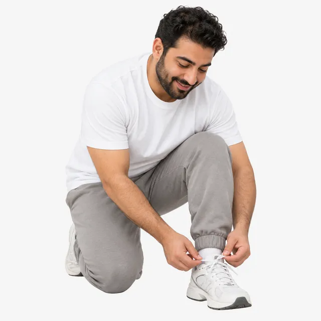 A smiling man in gray joggers kneeling to tie his running shoe