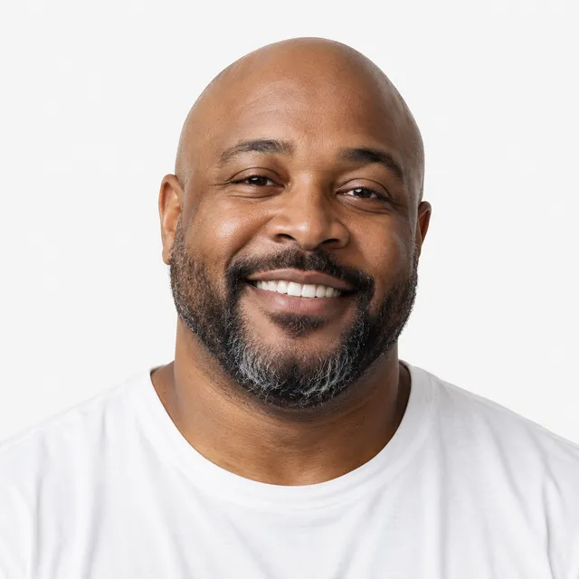 A smiling bald man with a graying beard in a white T-shirt
