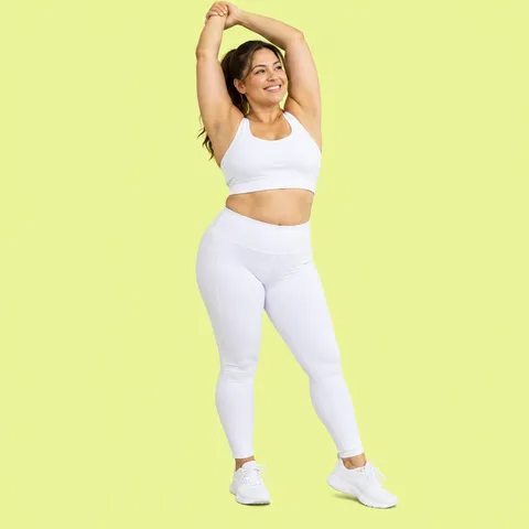 A smiling woman stretching her arms overhead in white activewear