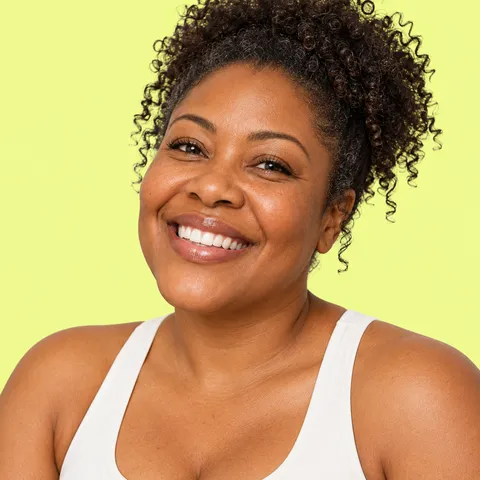 A smiling woman with curly hair pinned up, in a white tank top